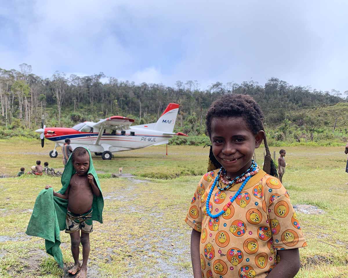 A child grinning in front of an MAF plane in Mokndoma, Papua